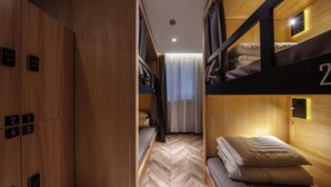 Une chambre d’hôtel compacte avec un lit superposé, une armoire avec des compartiments numérotés et un sol à motifs en chevrons.