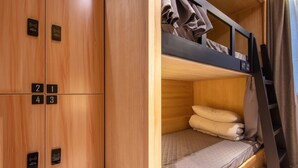 Un lit superposé avec une tête de lit en bois et un lit simple en dessous. Il y a quatre casiers numérotés accrochés au mur.