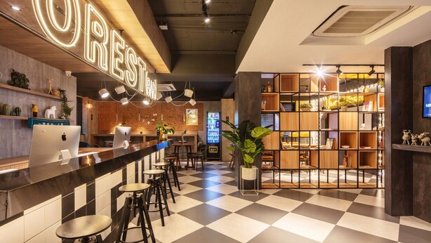Un espace bar avec un sol à carreaux, un comptoir avec des tabourets et une bibliothèque agrémentée d’un néon.