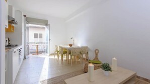A modern kitchen with white cabinets, a dining area with a white table and chairs, and a small seating area with a candle and a plant.
