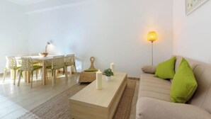 A living room with a sofa, a coffee table, a dining table with chairs, and a wall-mounted lamp.