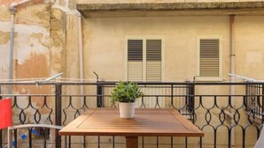 A rooftop terrace with a wooden table, a potted plant, and a red chair.