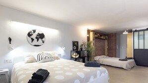 A modern bedroom with a large bed, a smaller bed, a world map wall art, a bookshelf, and a brick accent wall.