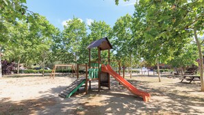 A playground with a slide and climbing area, surrounded by trees and a picnic table.