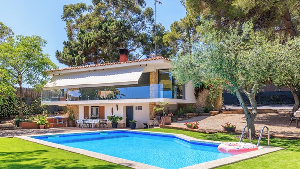 A two-story house with a swimming pool, outdoor seating, and a garden.
