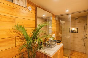 A bathroom with wooden walls, a sink with a large bowl, a mirror, and a shower area. - ELIVAAS House of Neptune 1 BHK Boutique (Morjim)
