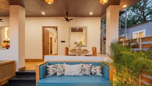 Eine Holzbank mit blauer Sitzauflage und gemusterten Kissen, ein Holztisch mit Blumen in einer Vase und ein großer Spiegel an der Wand.