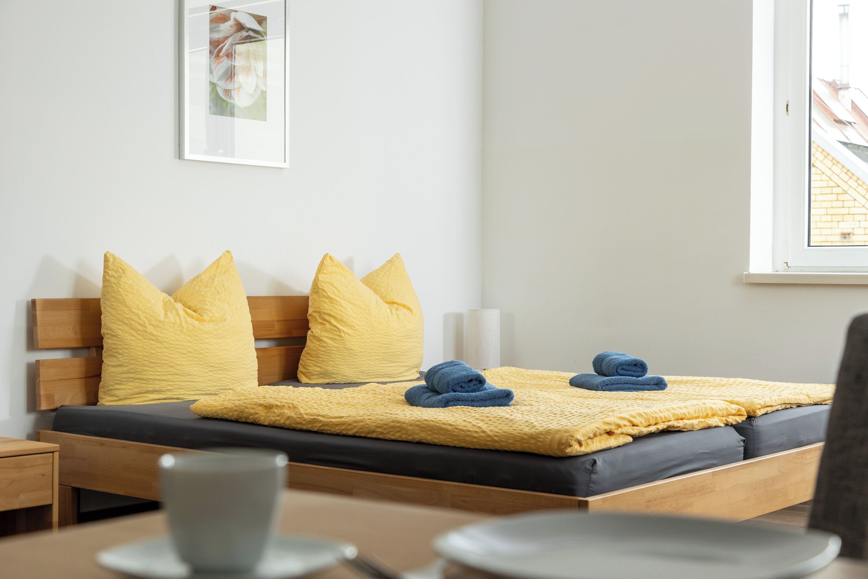 A neatly made bed with yellow pillows, a blue towel, and a yellow blanket.