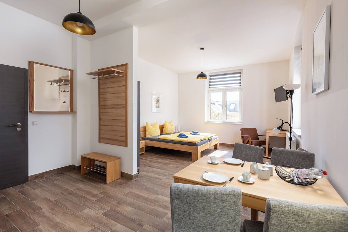 Une chambre moderne comprenant un lit, une table à manger avec des chaises, un bureau et une grande fenêtre.