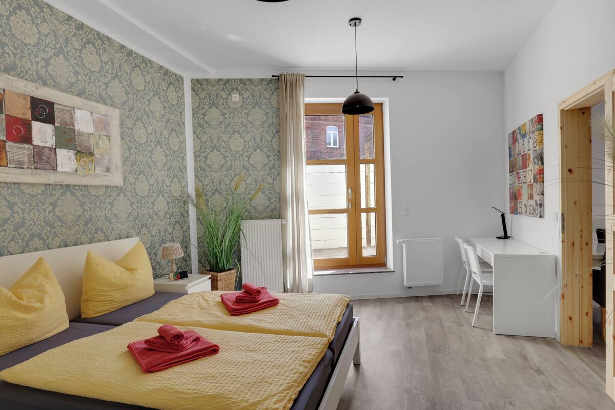 Une chambre moderne avec deux lits, un bureau et une vue sur un bâtiment en briques, visible par la fenêtre.