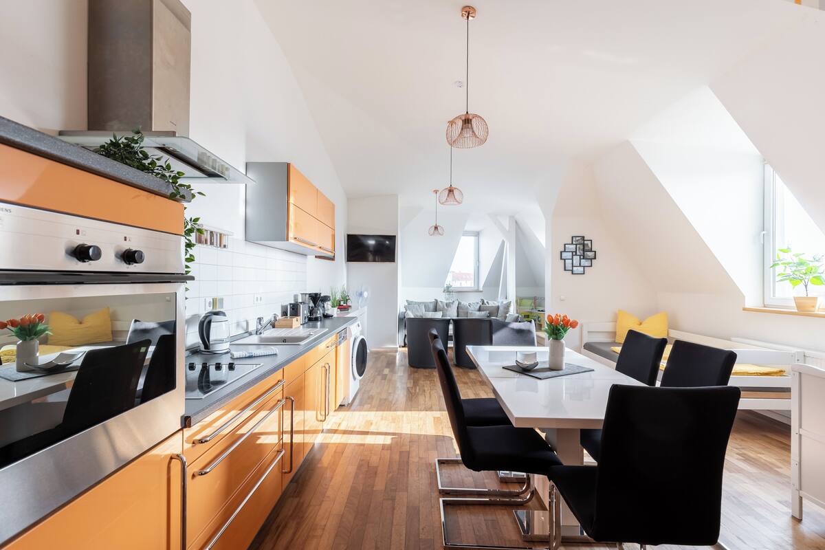 Une cuisine moderne dotée d’un îlot central, d’appareils électroménagers intégrés et d’un coin repas avec une table et des chaises hautes.