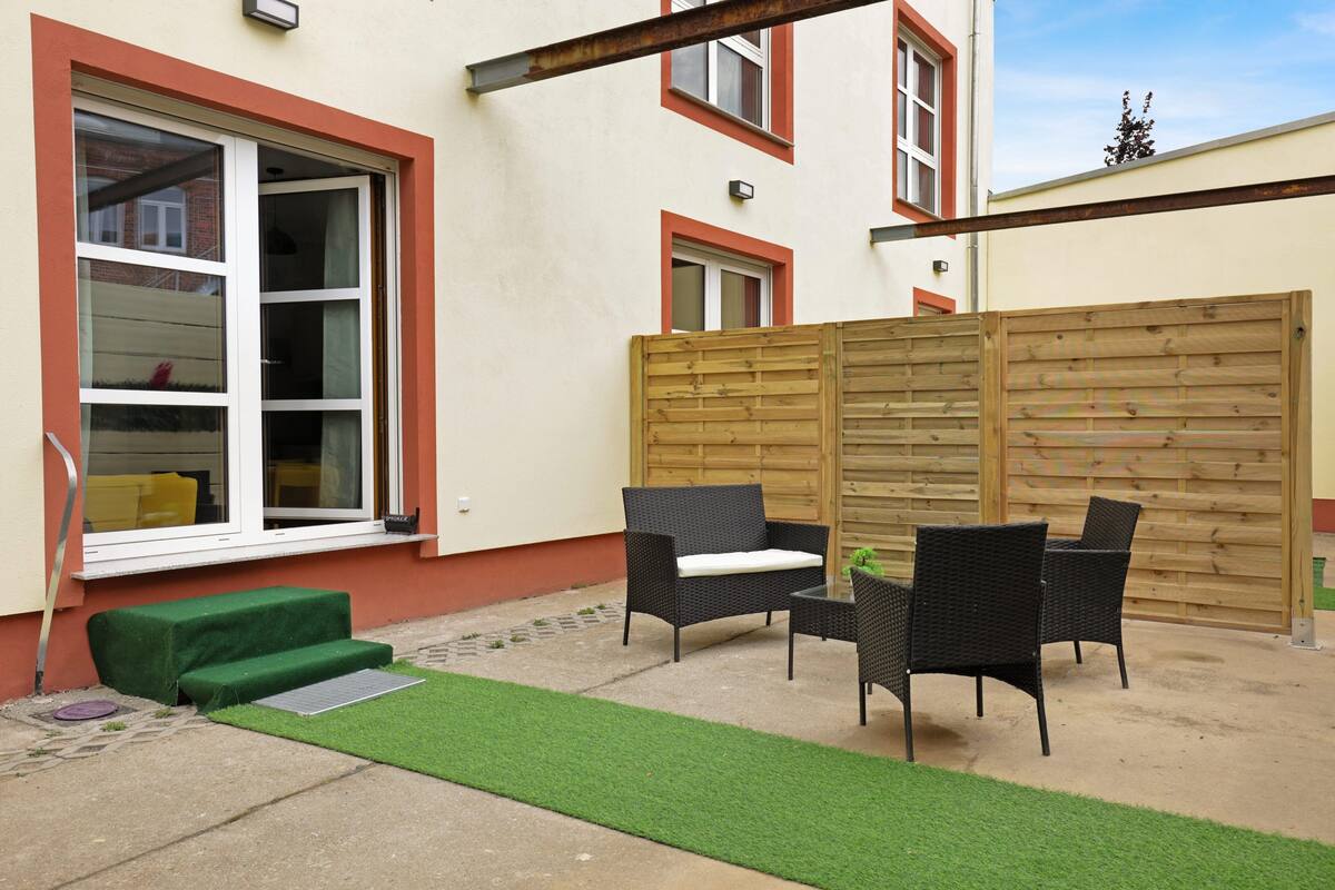 Une terrasse avec des meubles d’extérieur, un espace recouvert d’une pelouse artificielle et une clôture en bois.