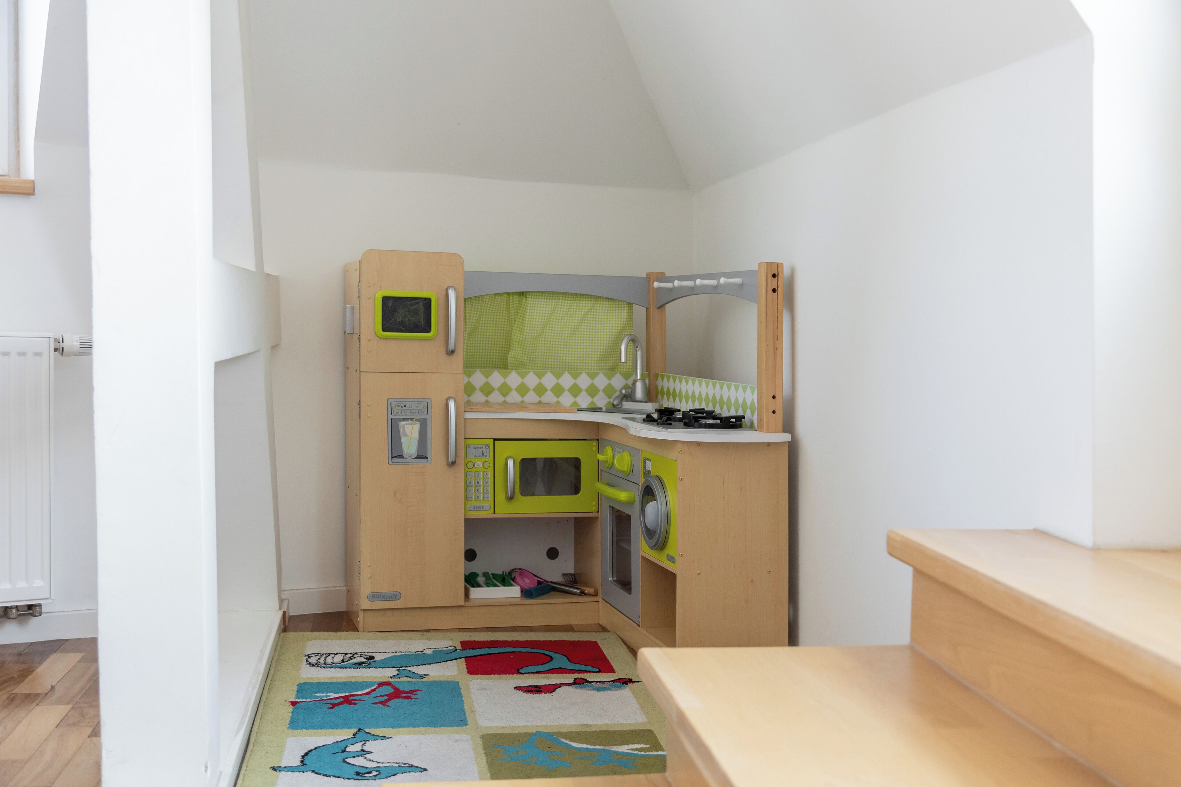 A compact kitchen with a microwave, oven, and sink, a small cabinet, and a colorful rug.