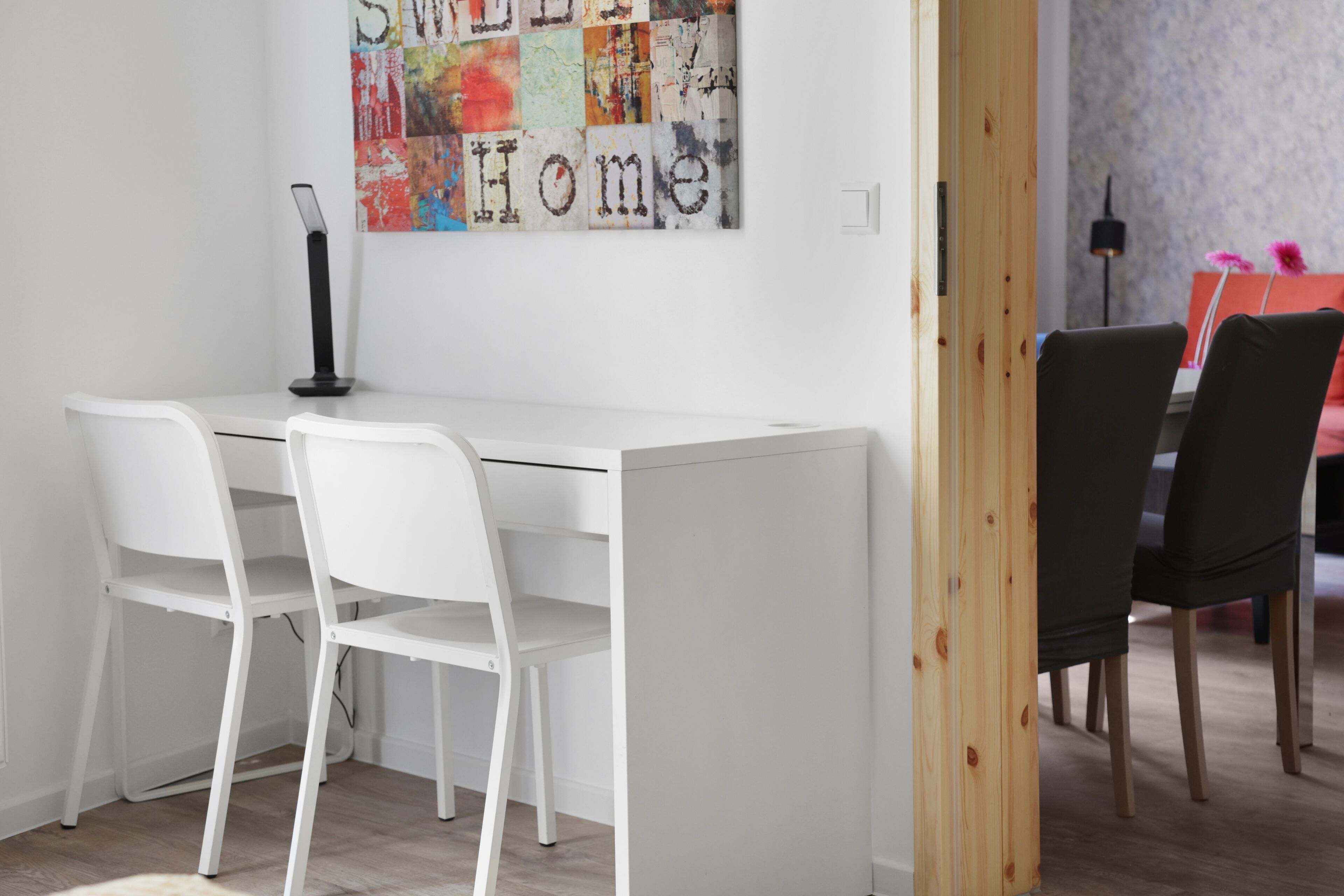 Un'area pranzo moderna con un tavolo e sedie bianche, un'opera d'arte astratta dai colori vivaci e una porta in legno.