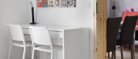 Un'area pranzo moderna con un tavolo e sedie bianche, un'opera d'arte astratta dai colori vivaci e una porta in legno.