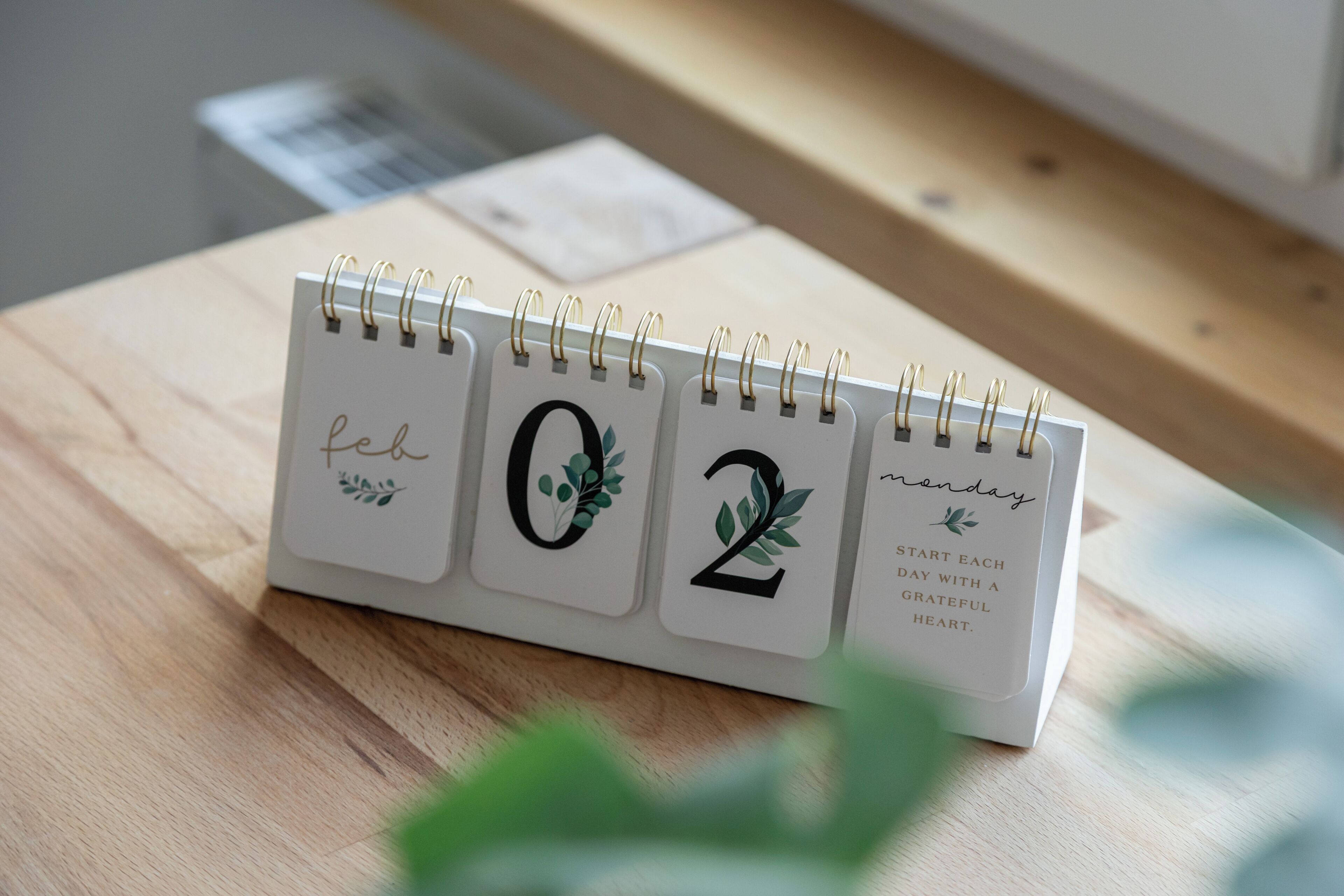 Un bureau sur lequel se trouve un agenda à spirale affichant la date « 02 » et le texte : « Commencez chaque journée avec un cœur reconnaissant. »