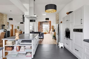 Une cuisine moderne avec des meubles blancs, un grand îlot central et un luminaire suspendu noir.