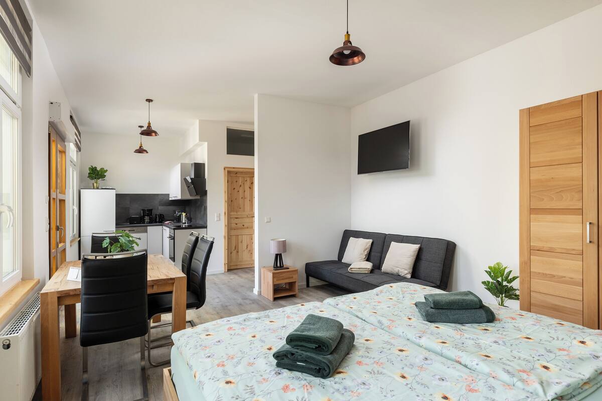Une chambre moderne et bien éclairée, équipée d’un lit, d’un bureau, d’une chaise, d’un canapé et d’un téléviseur.