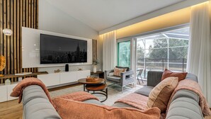 Un salon moderne doté d’un grand téléviseur à écran plat, de sièges confortables et offrant une vue dégagée grâce à de larges fenêtres.