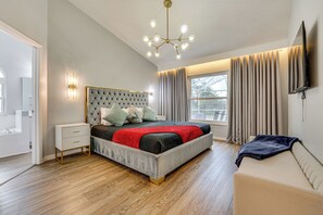 A modern bedroom with a large bed, bedside tables, a sofa, and a TV mounted on the wall.