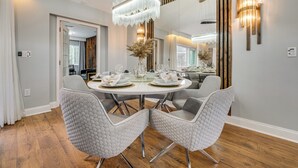 Un espace repas moderne avec une table ronde dressée pour quatre personnes, entourée de fauteuils capitonnés, d’un lustre et d’un mur décoratif en bois.