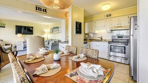 Una cocina moderna con electrodomésticos de acero inoxidable, un comedor con sillas de mimbre y una sala de estar con sofá y televisor.