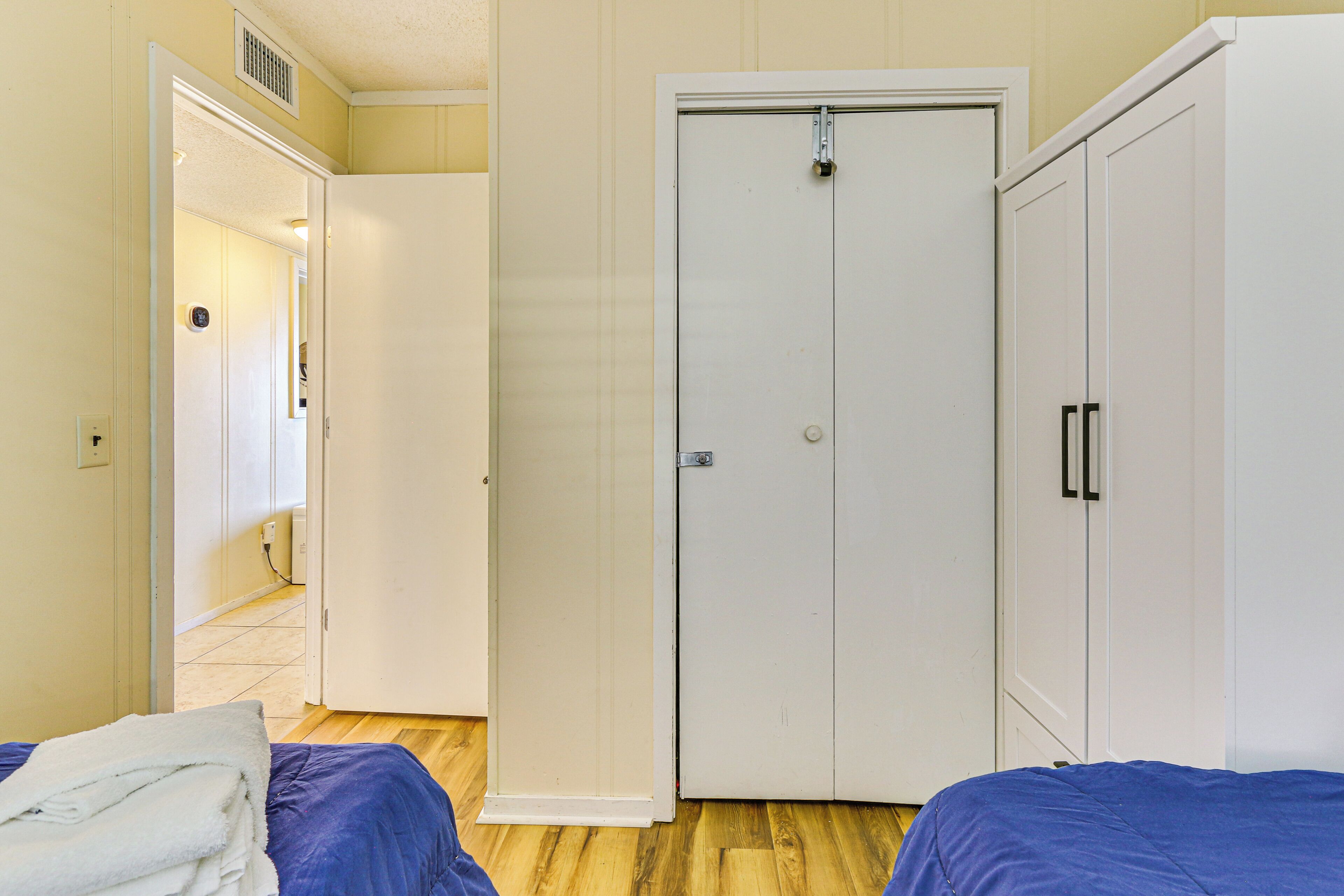 Une chambre avec deux lits, une armoire blanche et une porte donnant sur une autre pièce.