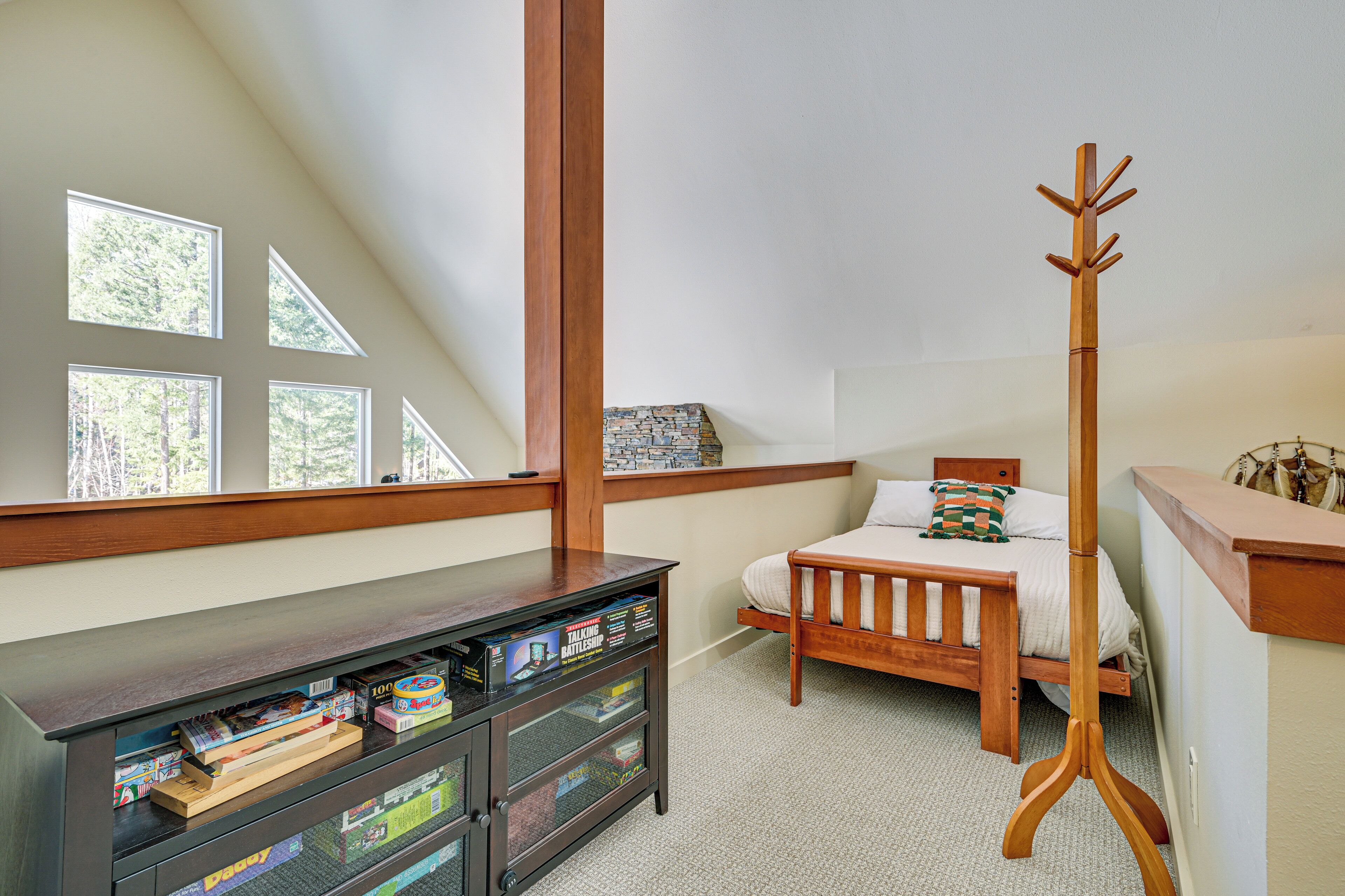 A bedroom with a sloped ceiling, a wooden bed, a nightstand, a wooden coat rack, and a window with a view of trees.