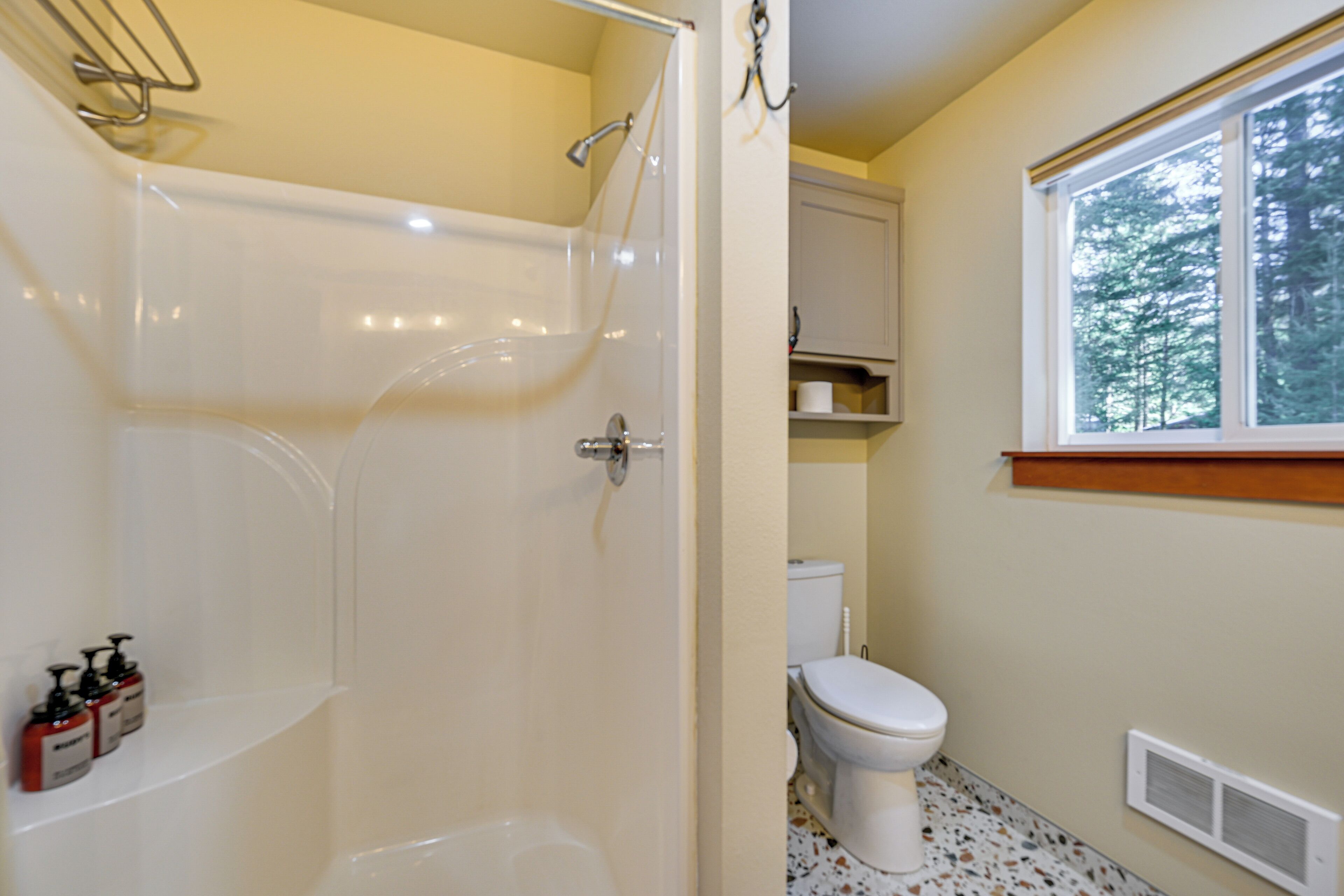 A bathroom with a bathtub, toilet, and a window with a view of trees.