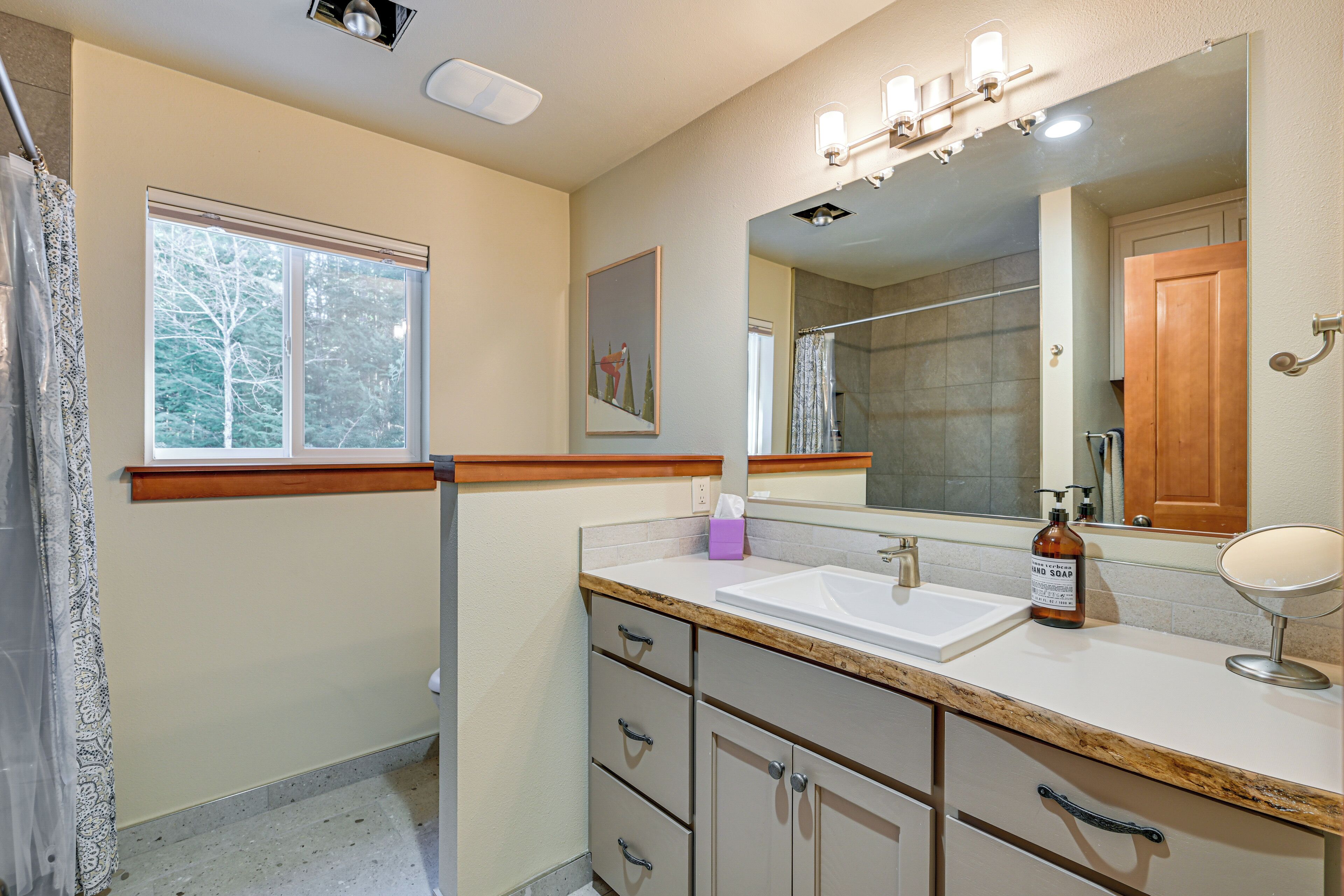 A bathroom with a large mirror, a sink, and a shower area.
