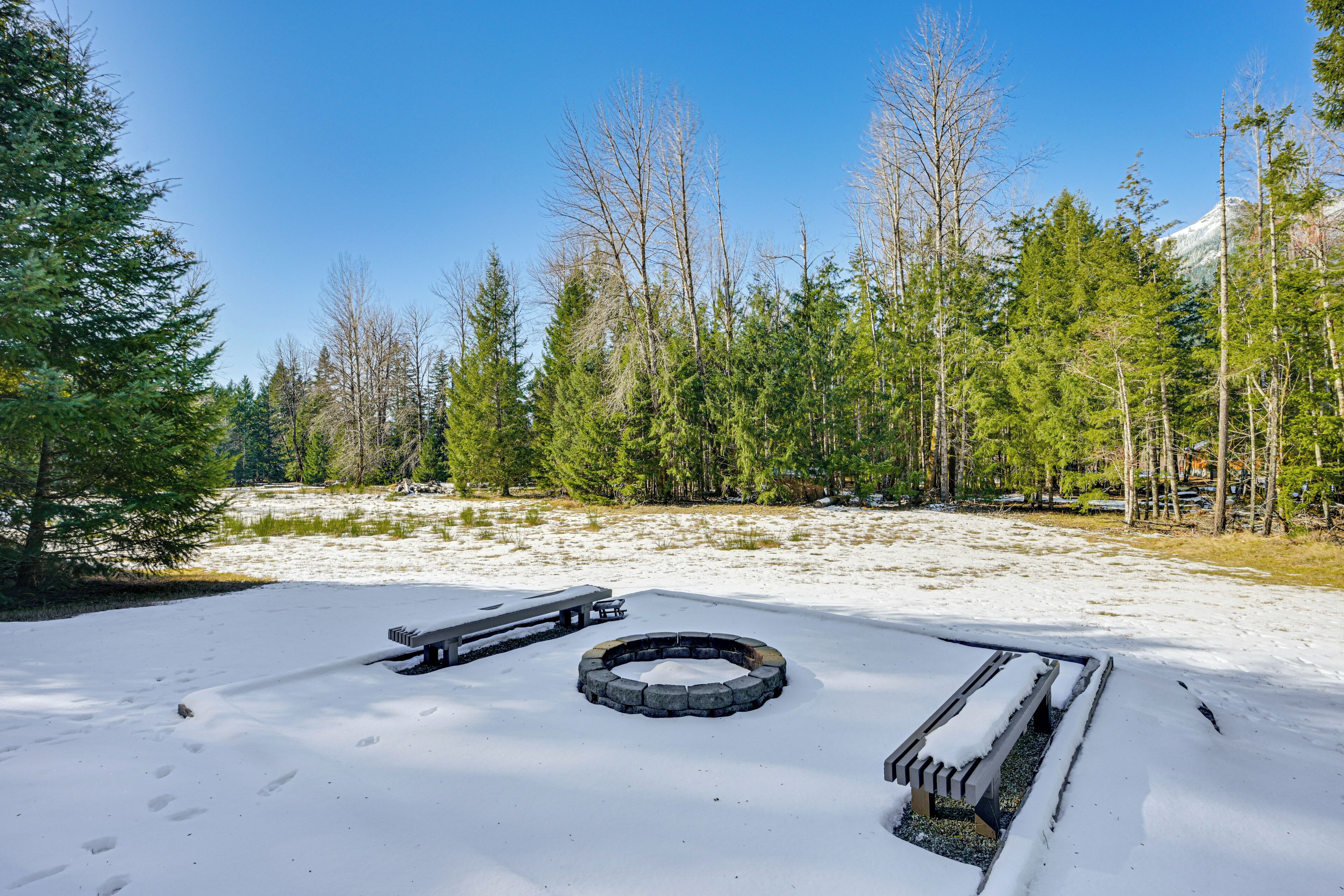A snow-covered outdoor area with a fire pit, picnic table, and benches.