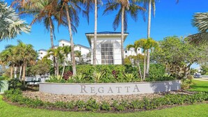 Un letrero con la palabra 'REGATTA' frente a un edificio de fachada blanca y una torre central, rodeado de palmeras y vegetación.