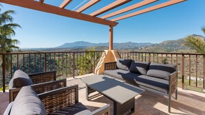 Ein Balkon mit einer Couch, Stühlen und einem Tisch, mit Blick auf eine Berglandschaft.