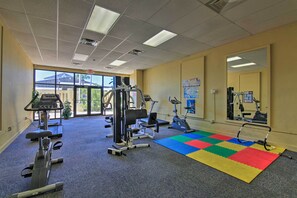 A gym with various exercise equipment, a colorful mat, and large windows. - Gulf-view Balcony: Beachfront Condo in Pcb! (Panama City Beach)