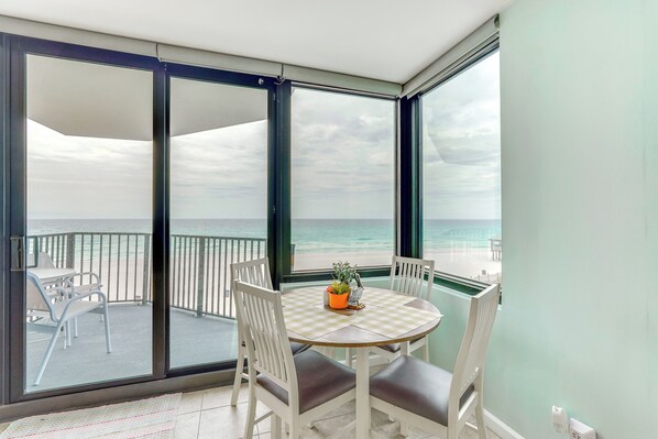 A balcony with a table and chairs, a view of the ocean, and a potted plant on the table.