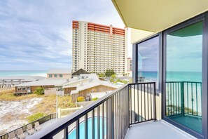A balcony with a view of the beach and ocean, a tall hotel building in the background, and a clear sky.