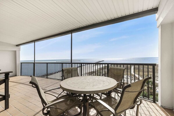A covered outdoor area with a round table and chairs, overlooking a beach.