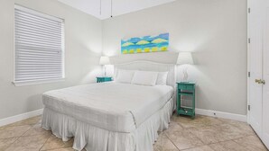 A bedroom with a bed, two bedside tables, a window with blinds, and a painting on the wall. - Grand Pointe 411, 3 bedrooms, 3 and a half baths, DIRECT BEACH FRONT (Orange Beach)