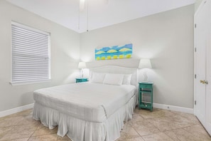 A bedroom with a bed, two bedside tables, a window with blinds, and a painting on the wall. - Grand Pointe 411, 3 bedrooms, 3 and a half baths, DIRECT BEACH FRONT (Orange Beach)