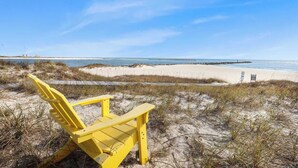 A beach chair on a sandy dune with a view of the ocean and a distant pier. - Grand Pointe 411, 3 bedrooms, 3 and a half baths, DIRECT BEACH FRONT (Orange Beach)