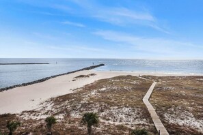 A beach with a wooden boardwalk leading to the water, sandy dunes, and a rocky breakwater.