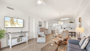 A spacious living room with a television, a sofa, a coffee table, and a dining area with chairs. - Grand Pointe 512 | 5th Floor Gulf-Front Condo w/ Panoramic Views & (Orange Beach)