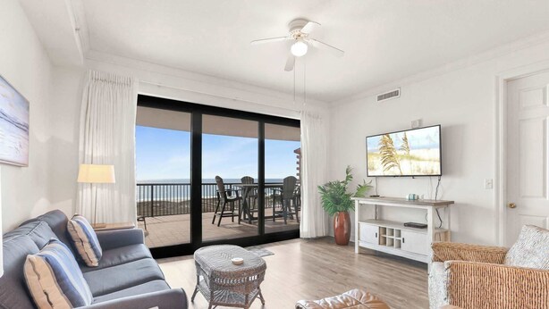 A spacious living room with a large sliding glass door leading to a balcony, a television, and a comfortable seating area. - Grand Pointe 512 | 5th Floor Gulf-Front Condo w/ Panoramic Views & (Orange Beach)