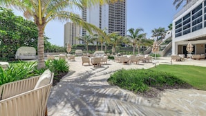 A resort with outdoor seating, palm trees, and a building with large windows. - Condo at Amrit Ocean Resort w/ Panoramic Views (Singer Island)
