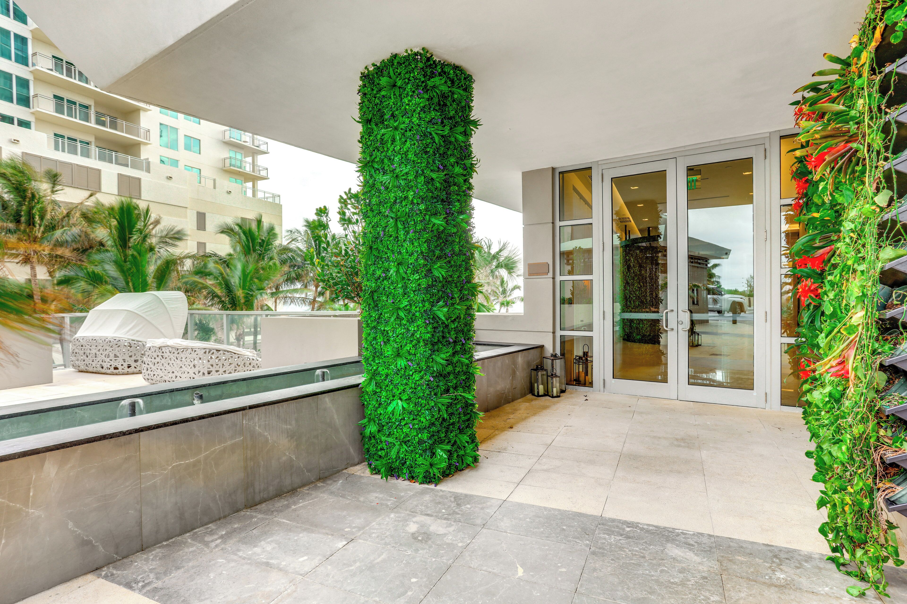A modern hotel with a vertical garden feature, a seating area with a white chair, and a glass door entrance.