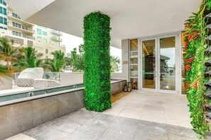 Un hôtel moderne doté d’un jardin vertical, d’un coin salon avec un fauteuil blanc et d’une entrée avec une porte en verre.