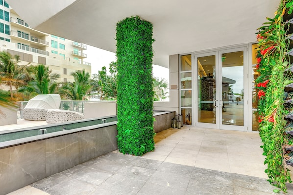 Un hotel moderno con un jardín vertical, un área de descanso con una silla blanca y una entrada con puerta de vidrio.