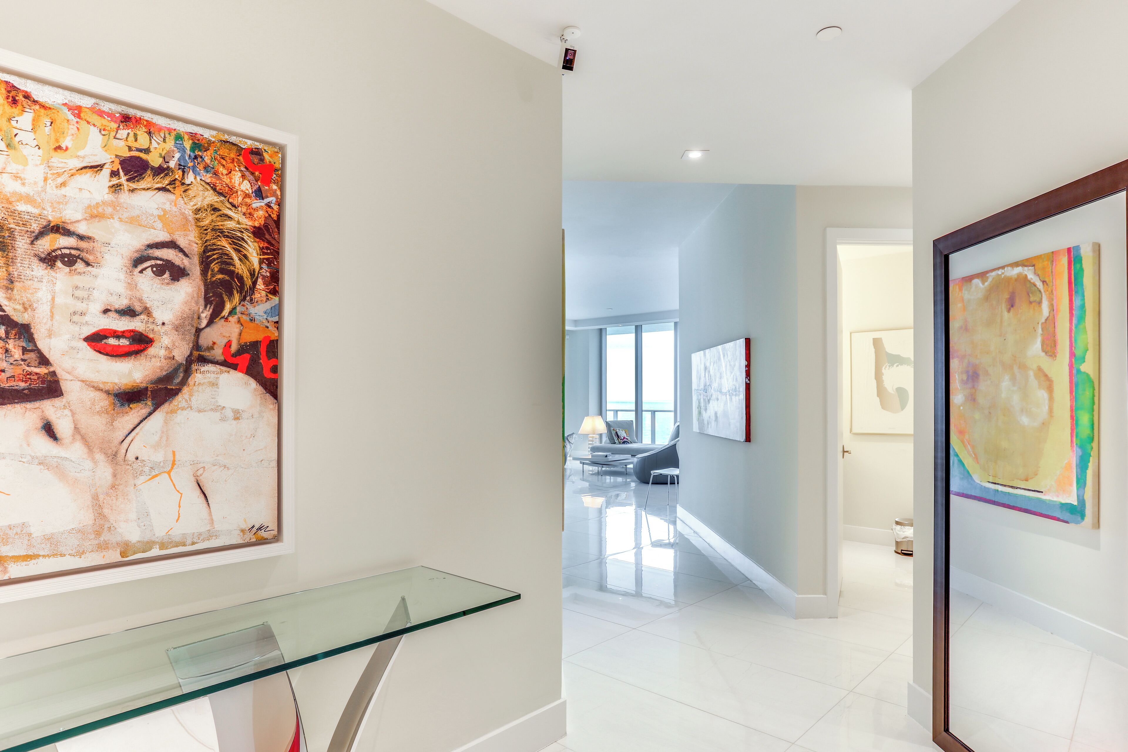 A modern interior with a glass display case, a large abstract painting, and a well-lit hallway leading to a seating area.