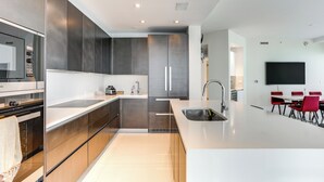 A modern kitchen with stainless steel appliances, a large island, and red chairs in the dining area. - Condo at Amrit Ocean Resort w/ Panoramic Views (Singer Island)