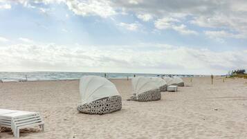 A beach with covered seating areas and a view of the ocean.